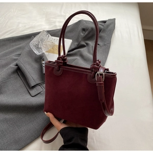 Detail of burgundy suede bucket bag with knotted handle and embossed brand logo