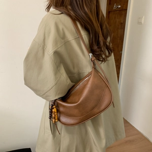Detail of vintage brown half-moon crossbody bag with wooden bead charm on shoulder strap