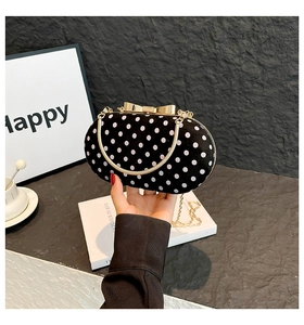 Close-up of velvet polka dot clutch bag featuring a gold bow buckle and chain strap