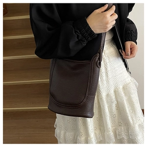 Close-up of deep coffee lychee pattern leather bucket bag on wooden stairs