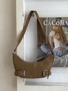 Brown suede crescent shoulder bag with metallic buckle details and adjustable strap