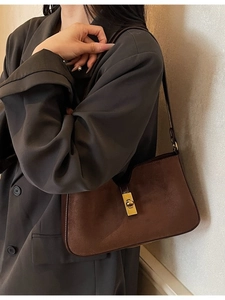 Sac seau vintage en daim marron foncé avec fermoir doré porté par un modèle