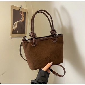 Detail of dark brown suede bucket bag featuring knotted handles and floral embossed logo
