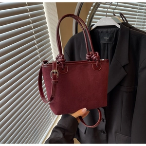 Detail of burgundy suede bucket bag with knot handle and adjustable shoulder strap