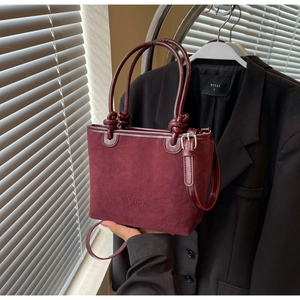 Close-up of wine red suede bucket bag featuring knot decorative handle and embossed logo