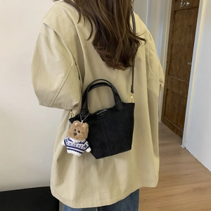 Detail view of a matte black suede bucket bag with a cute bear charm on a model