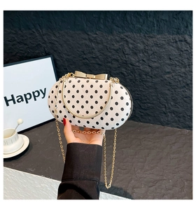 Chic polka dot handbag with a large gold bow clasp and metallic chain strap shown in detail