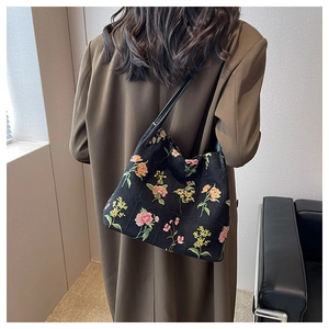 Detail of floral embroidery on a black shoulder bucket bag worn with a brown coat