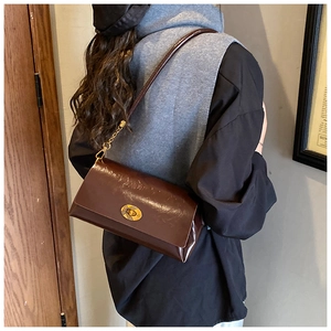 Détail du sac bandoulière en cuir brillant marron foncé avec fermoir rotatif doré