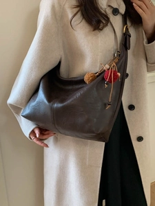Dark brown leather hobo bag with pompom charm worn with a classic beige winter coat