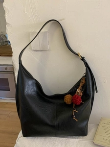 Minimalist black large hobo bag with a colorful ethnic charm against a white wall