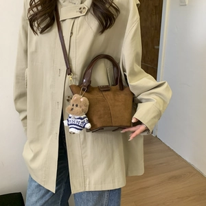 Detail view of a brown frosted bucket bag with a teddy bear charm and sleek shoulder strap