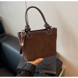 Close-up of brown suede bucket bag with embossed floral logo and knot detail strap
