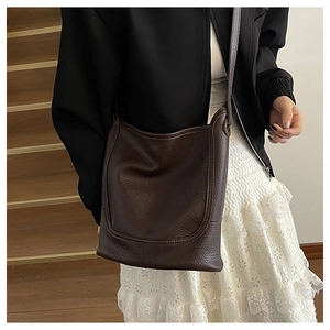 Detailed view of dark brown litchi leather shoulder bag worn by a model on stairs