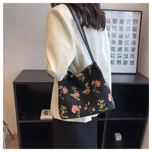 Detailed view of colorful floral embroidery on a black canvas bucket bag with shoulder strap