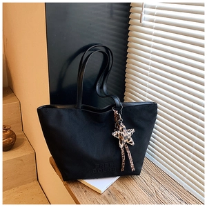 Close-up of black tote bag with embossed logo and leopard star charm on a wooden bench
