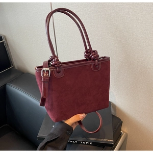 Detail of burgundy suede bucket bag with knotted handle and embossed floral logo