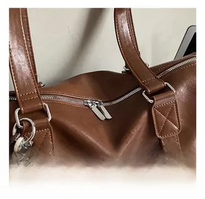 Close-up of brown leather travel tote showing dual metal zippers and stitching details