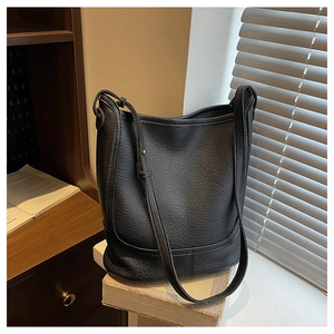 Close-up of black lychee grain leather bucket bag with adjustable strap on bookshelf