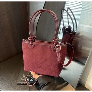 Close-up of burgundy suede and patent leather handbag with floral logo detail