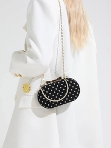 Elegant black polka dot handbag with gold chain strap shown on a white blazer outfit