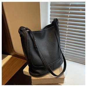 Close-up of black lychee grain leather bucket bag with detailed stitching on wooden desk