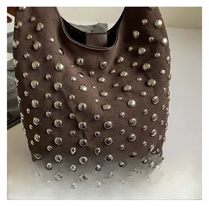 Dettaglio ravvicinato delle borchie punk vintage su una borsa a secchiello in camoscio marrone