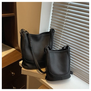 Detailed macro of two black lychee grain leather bucket bags on a vintage bookshelf