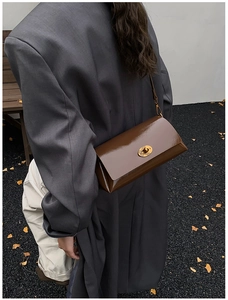 Détail du sac à bandoulière en cuir verni marron foncé avec fermoir doré sur un costume