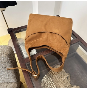 Détail du sac cabas en daim fauve avec coutures incurvées sur une table en verre vintage