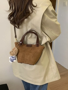 Brown suede bucket bag with leather handle and cute bear charm shown on model