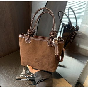 Detail view of dark brown suede bucket bag with braided handle on a black book