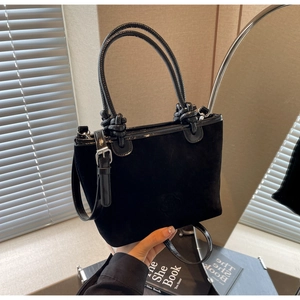 Detail of black suede bucket bag with braided knot handle and embossed logo design