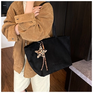 Detail of black suede tote bag featuring embossed logo and a leopard star charm