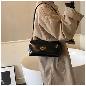 Détail du sac bandoulière en cuir noir brillant avec un fermoir tournant ovale doré