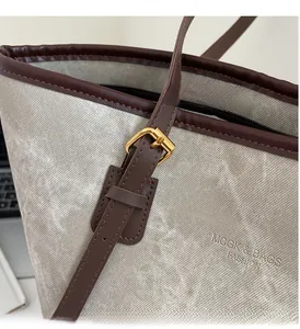 Detail of shimmering grey tote bag featuring gold hardware and brown leather strap