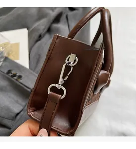 Detail of silver metal hook and leather strap connection on brown box handbag