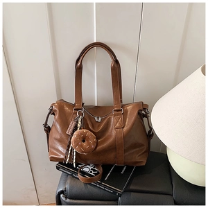 Brown faux leather tote bag with cute charms and metal zippers on a leather bench