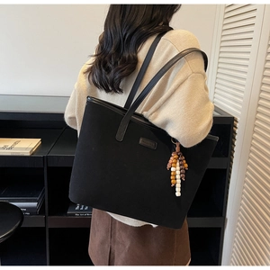 Close-up of matte black tote bag with wooden bead charm and long leather shoulder straps