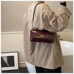 Détail d'un sac à bandoulière rouge foncé brillant avec fermoir rotatif doré sur tenue