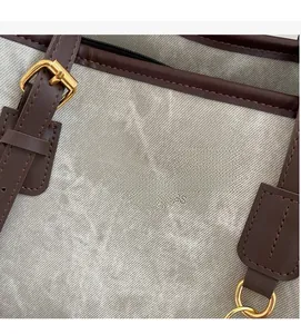 Close-up of textured grey tote fabric with brown leather strap and gold buckle detail