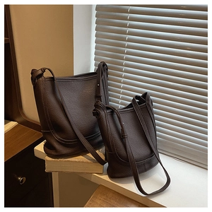 Two sizes of brown pebble leather bucket bags stacked on books by a window with natural light