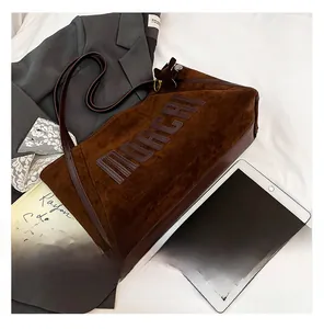 Detail of brown suede tote bag with embossed MOAGRI text and leather handle in a workspace