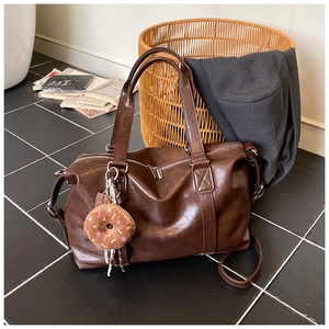 Detail of a dark brown large travel tote bag with glossy finish and plush donut charm