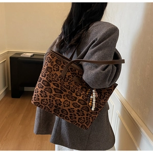 Detail of leopard print tote bag with brown leather strap and beaded charm on shoulder