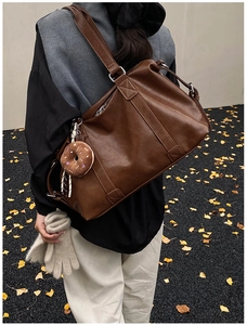 Deep brown leather tote bag detail with donut plush charm on model in autumn street