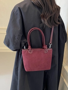 Burgundy suede tote bucket bag with embossed floral logo and adjustable shoulder strap