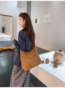 Sac à bandoulière hobo en daim marron avec grande poche avant porté par un mannequin