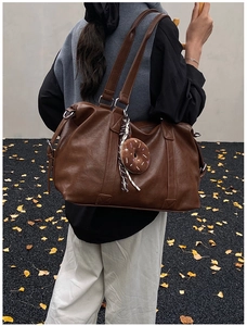 Detail of dark brown leather tote bag with donut pendant on autumn ginkgo leaves