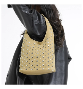 Dettaglio della borsa a tracolla in pelle scamosciata beige con rivetti e giacca nera